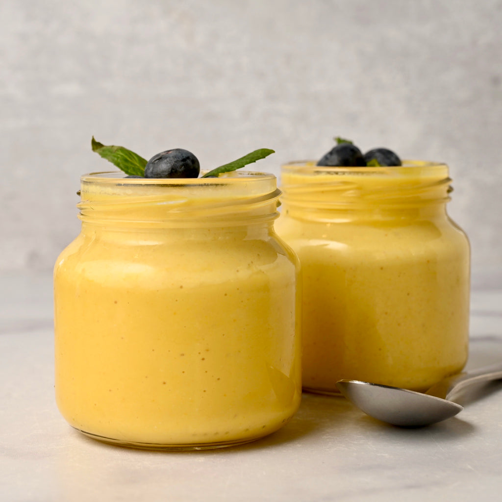 A close up of a clear glass jar filled with mango cashew pudding and topped with blueberries