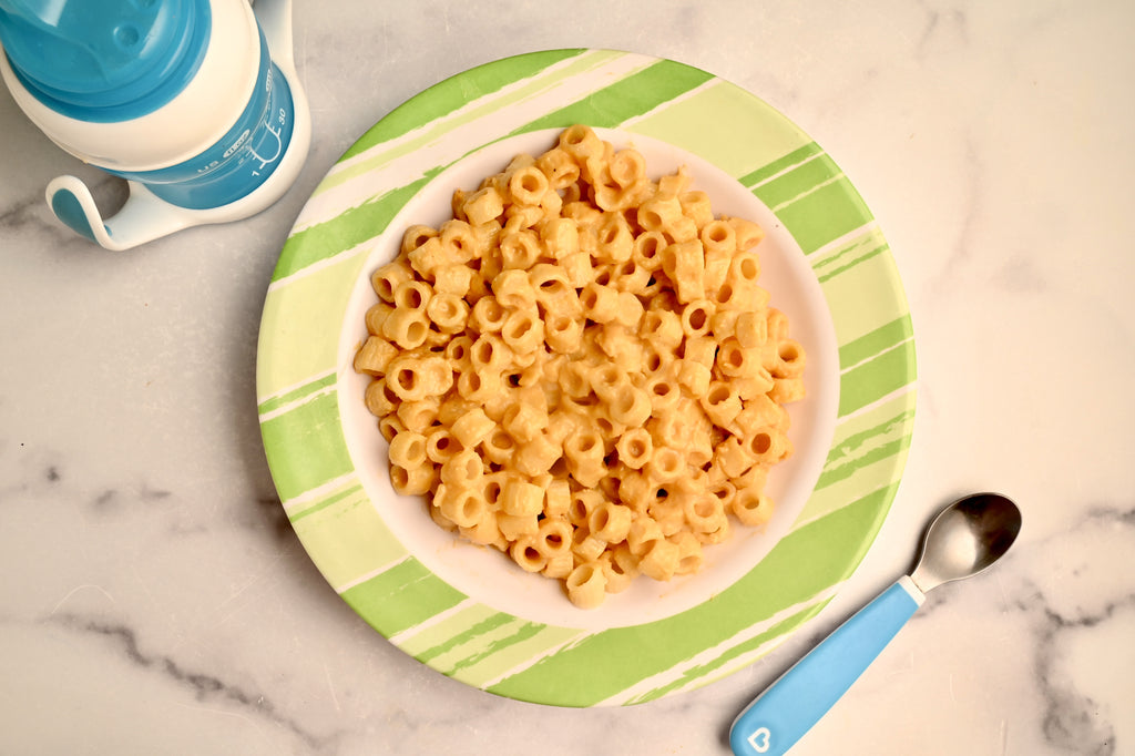 A plate of cheesy noodles with a sippy cup next to it