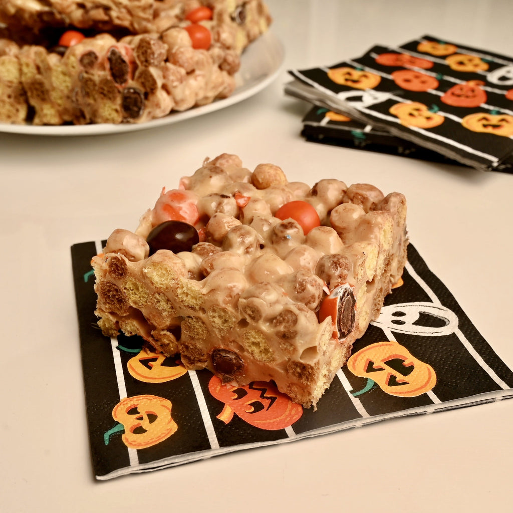 A plate of peanut butter cereal bars with black and orange M and M candies
