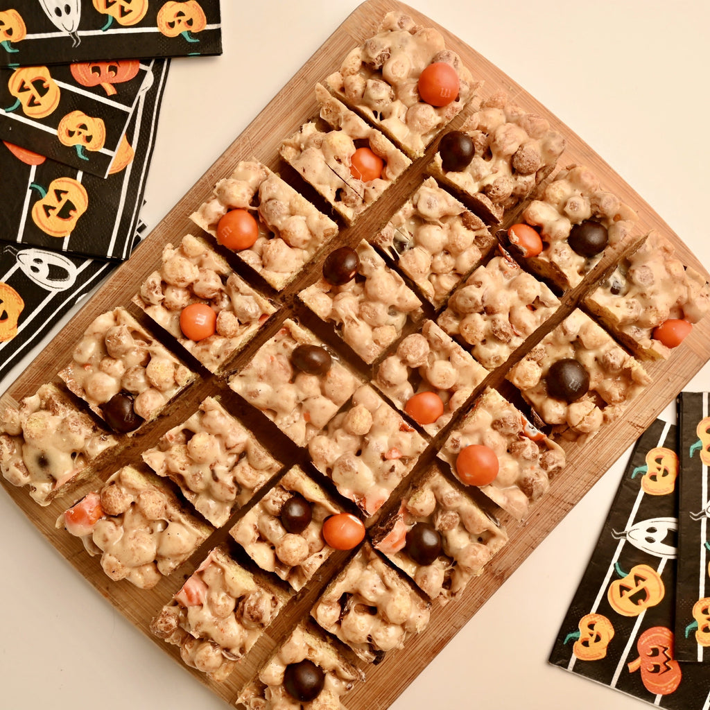 A row of sliced peanut butter cereal bars with black and orange M and M candies