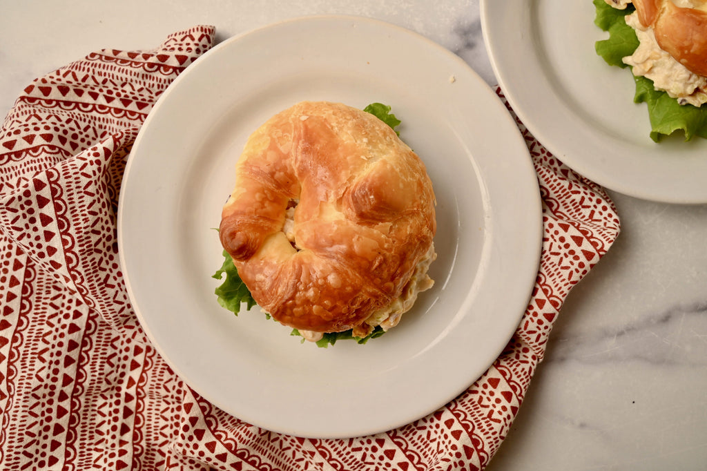 A white plate with a croissant sandwich in the middle of it