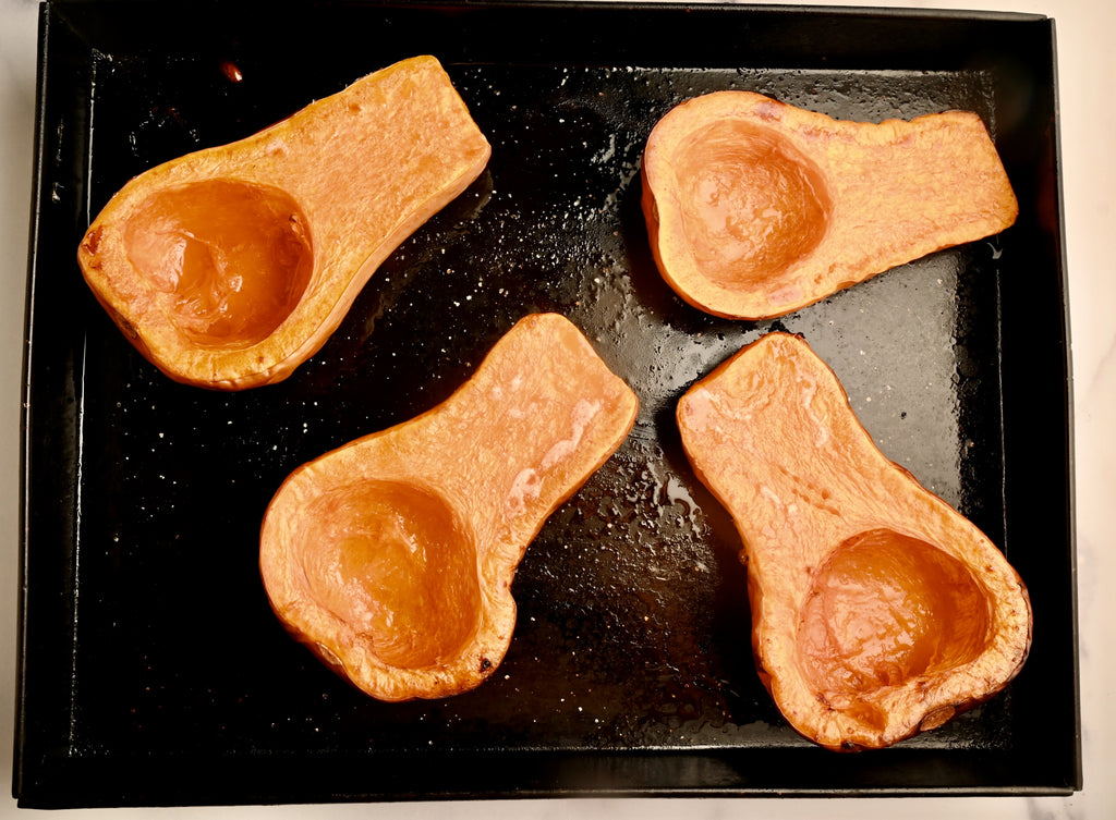 Halved roasted butternut squashes on a black cooking tray