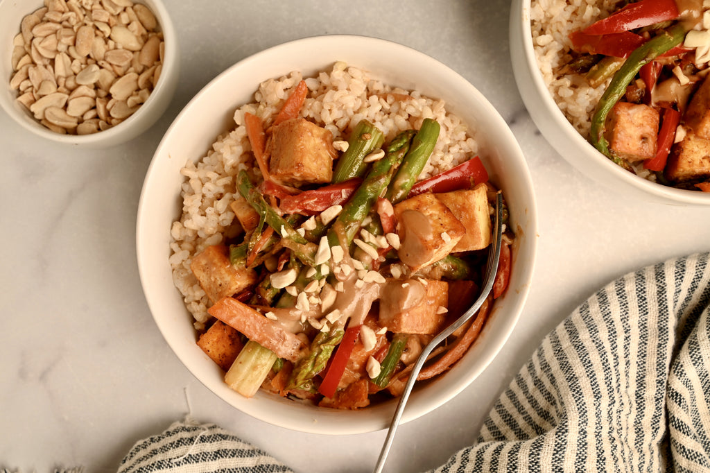 A bowl of tofu and asparagus stir fry in a white bowl with other vegetables