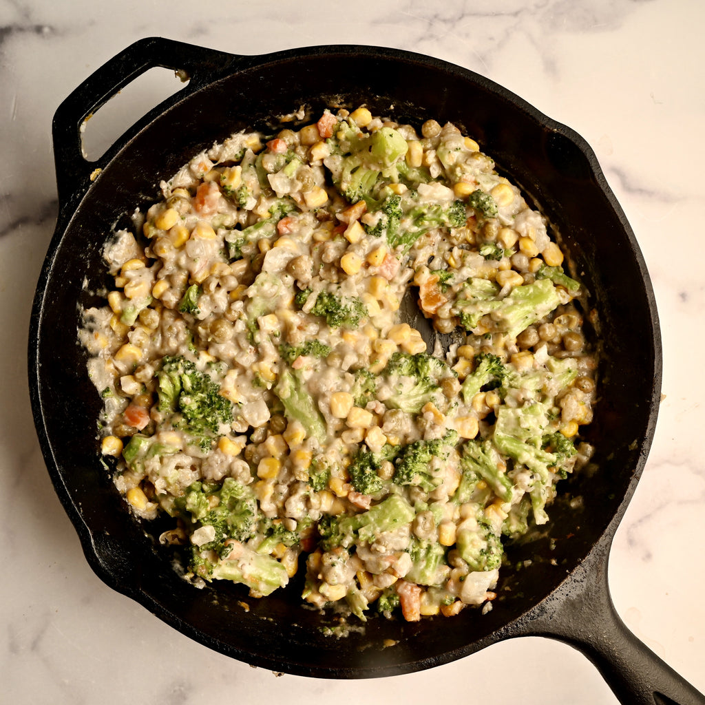 A black cast iron skillet with vegetables cooking in a cream sauce