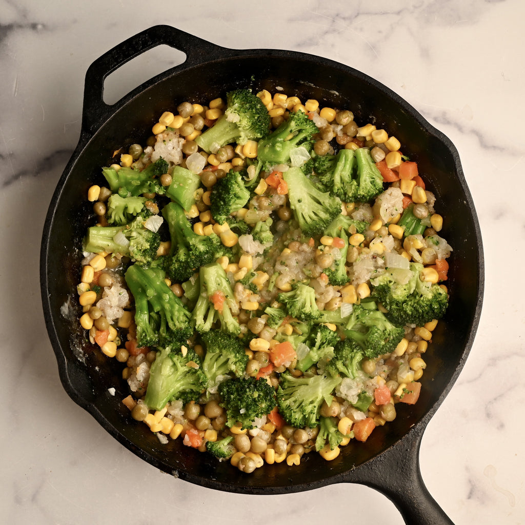 A black cast iron skillet with vegetables cooking in it