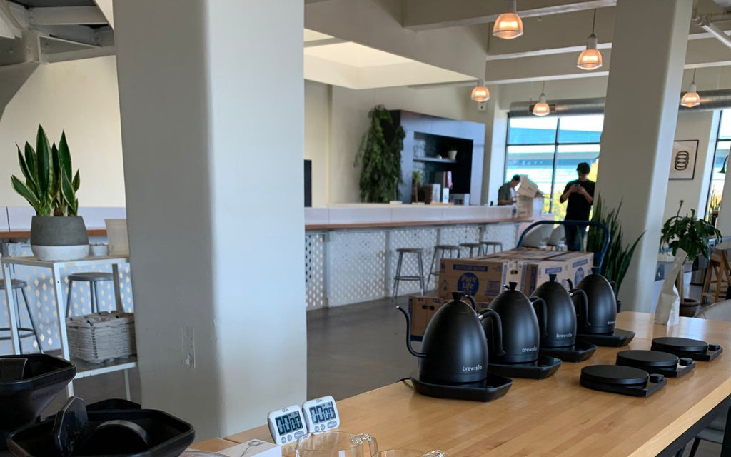 Brewista Artisan Gooseneck Kettles are sitting atop a wooden table to be used for Brewers Cup Competition.