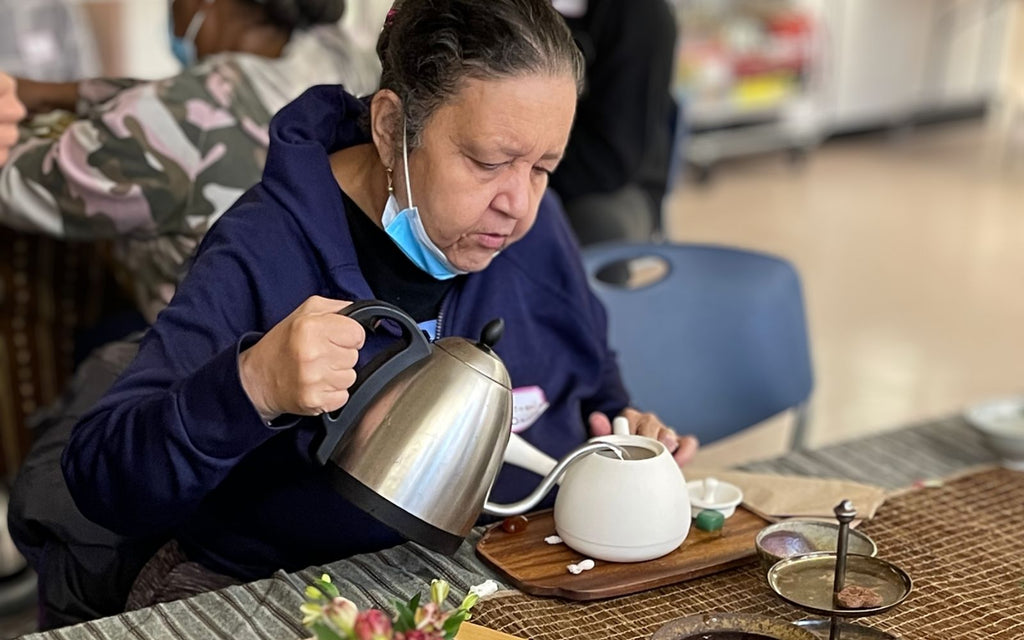 An older woman is pouring water into her teacup from a Bonavita kettle.