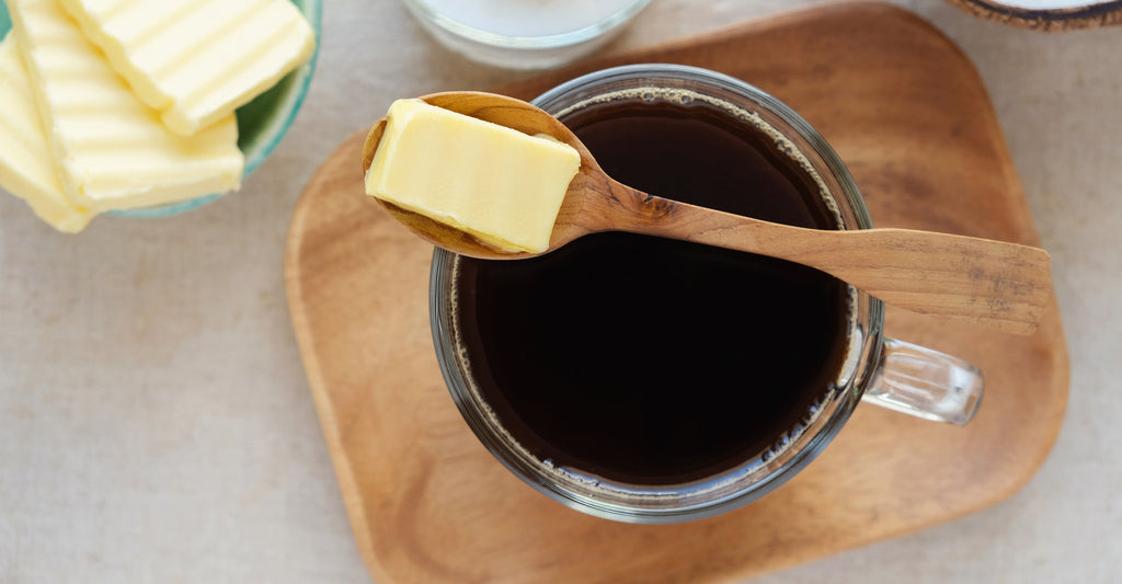 A spoonful of butter sits atop a mug filled with coffee.