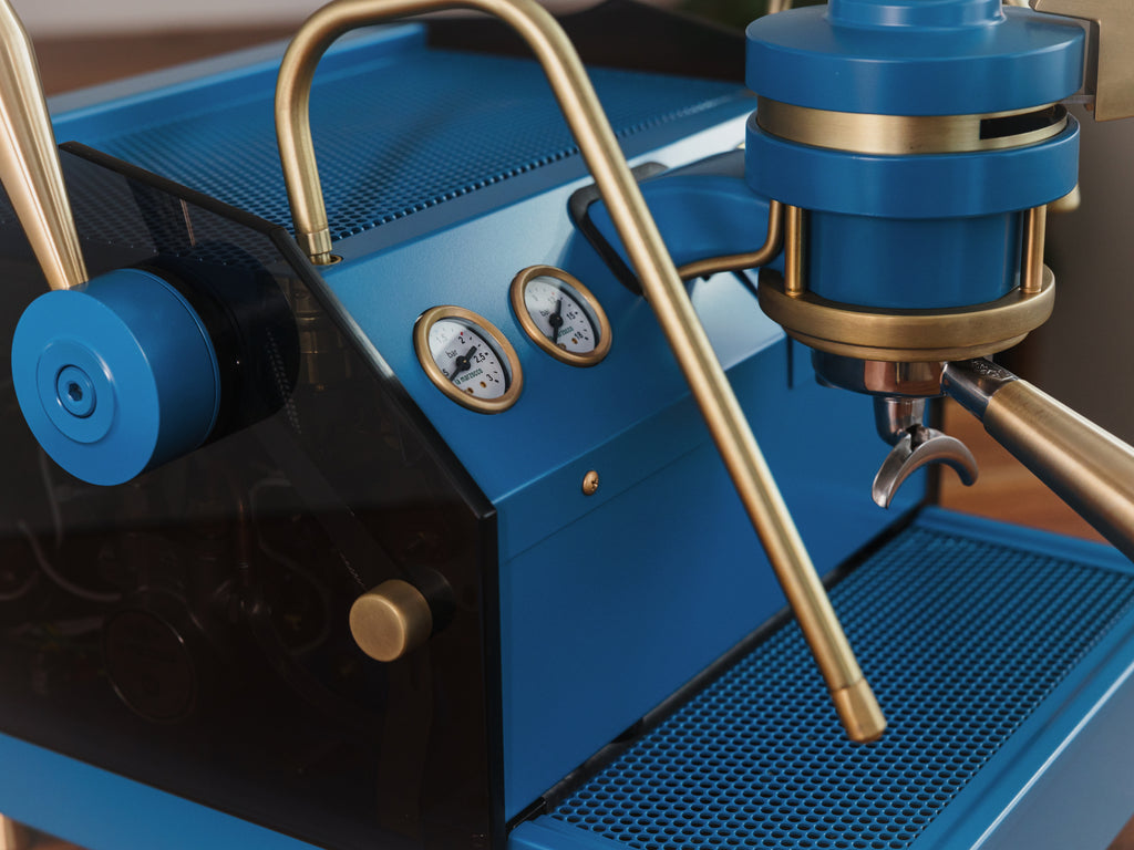 A blue Specht La Marzocco GS3 espresso machine with tinted, see-through glass side panels and polished brass finishes.