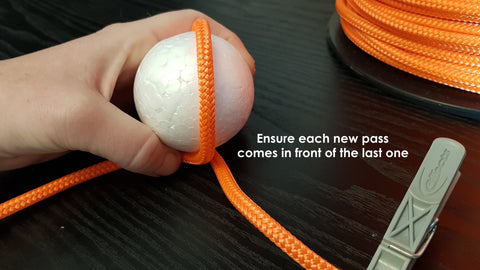 Orange rope is wrapped around a white ball to begin making a monkey fist