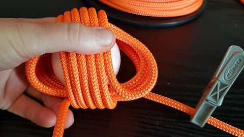 Multiple loops of orange rope are wrapped around a ball in their second layer to make a monkey fist