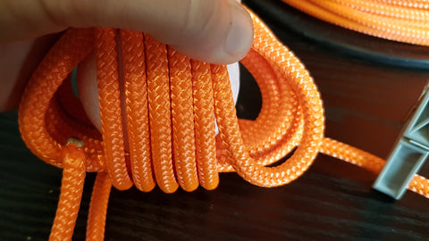 Multiple loops of orange rope are wrapped around a ball, beginning the third layer to make a monkey fist