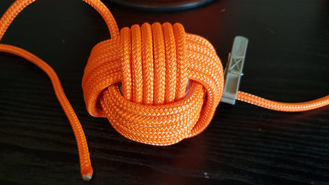 Multiple loops of orange rope are wrapped around a ball, finishing the third layer to make a monkey fist