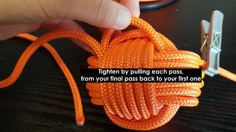 A hand pulls loops of orange rope tight to tidy up a DIY monkey fist
