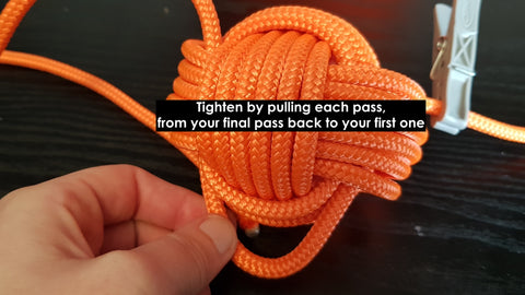 A hand pulls loops of orange rope tight to tidy up a DIY monkey fist