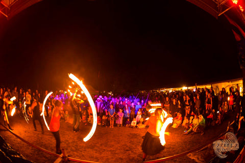 A group of people spin fire poi and fire staff at night while an audience watches