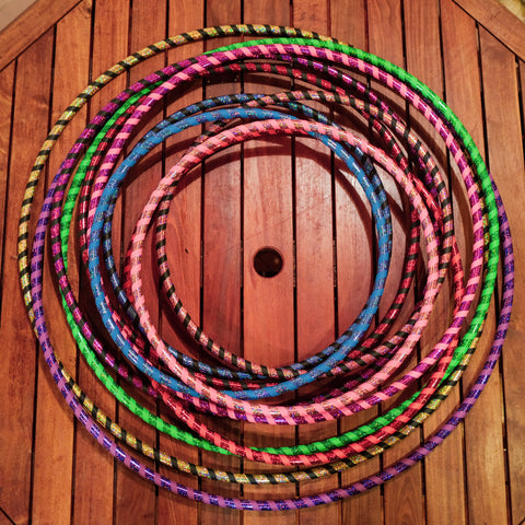 A stack of brightly coloured hula hoops sit against a dark wood background