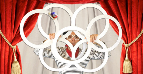 A person dresses as a mime holds multiple circus props in front of their face