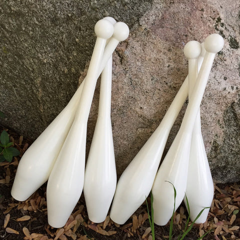 Six white juggling clubs sit against a rock on the grass