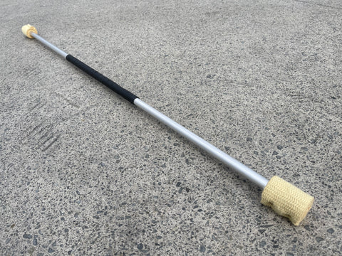 A fire spin staff with kevlar wick sits on a concrete backdrop