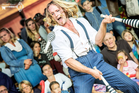 A man juggles enthusiastically with juggling clubs while an audience watches