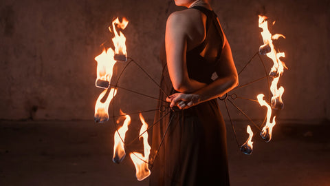 A person stands holding lit fire fans behind their back