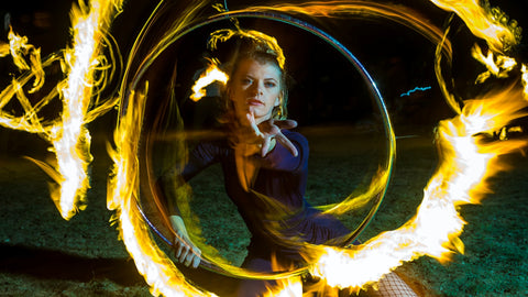 A person looks at the camera as they spin a fire hula hoop