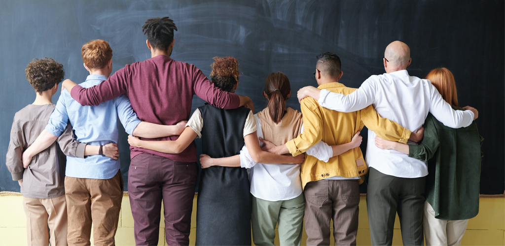 Diverse group of people hugging each other facing a blackboard.