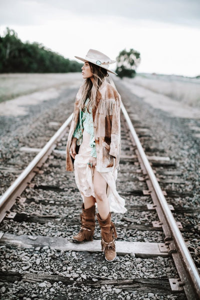 woman in ethnic western-inspired outfit with fringe jacket, boots and hat