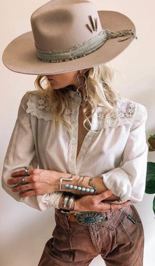 stylish woman in western outfit with white lace shirt, western belt, brown jeans, turquoise jewellery and beige hat