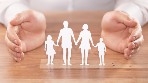 a woman hands around a paper cutout family protecting them on a wooden table