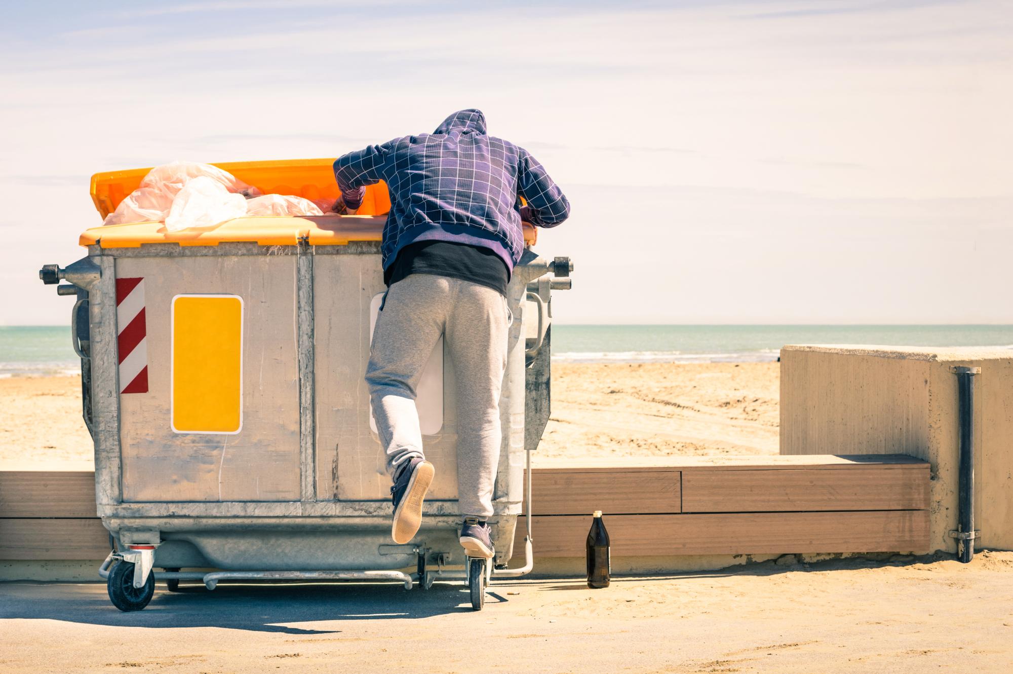 A person rummaging in trash container looking for food and reusable goods.