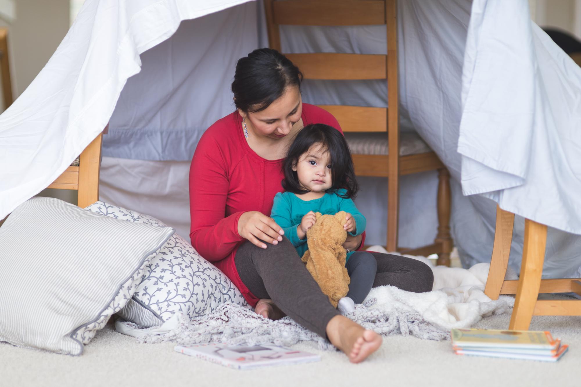 mom plays with her daughter under makeshift fort in living room