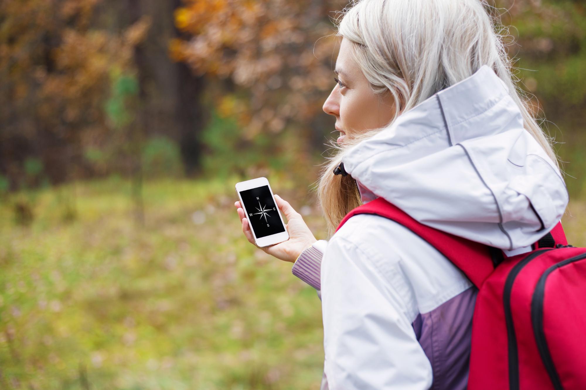 Woman checking compass app on her smartphone while hiking in forest.