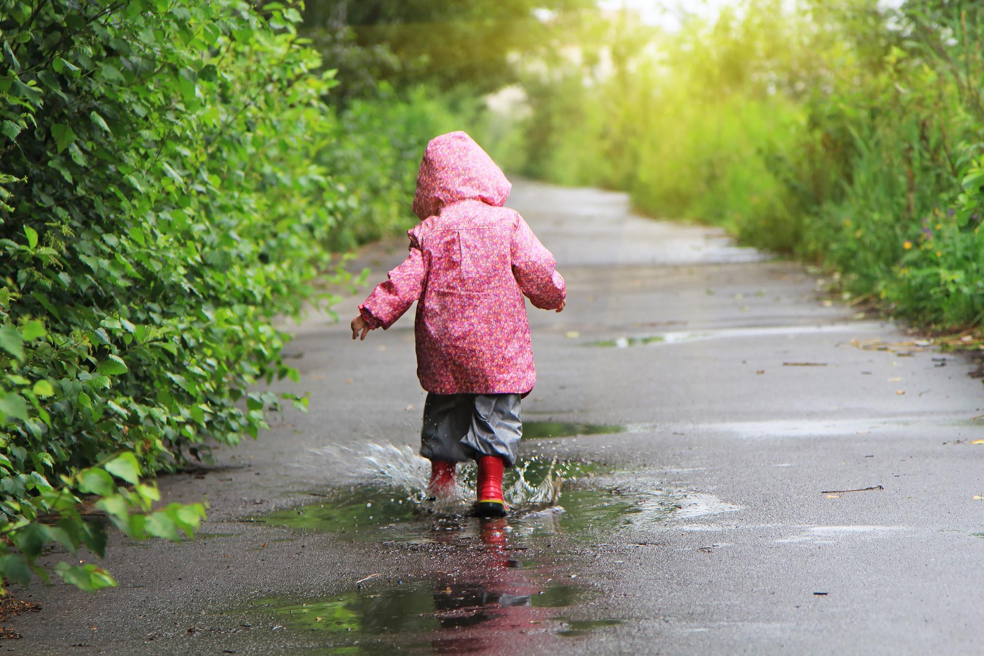 Toddler girl jumping in puddles after rain