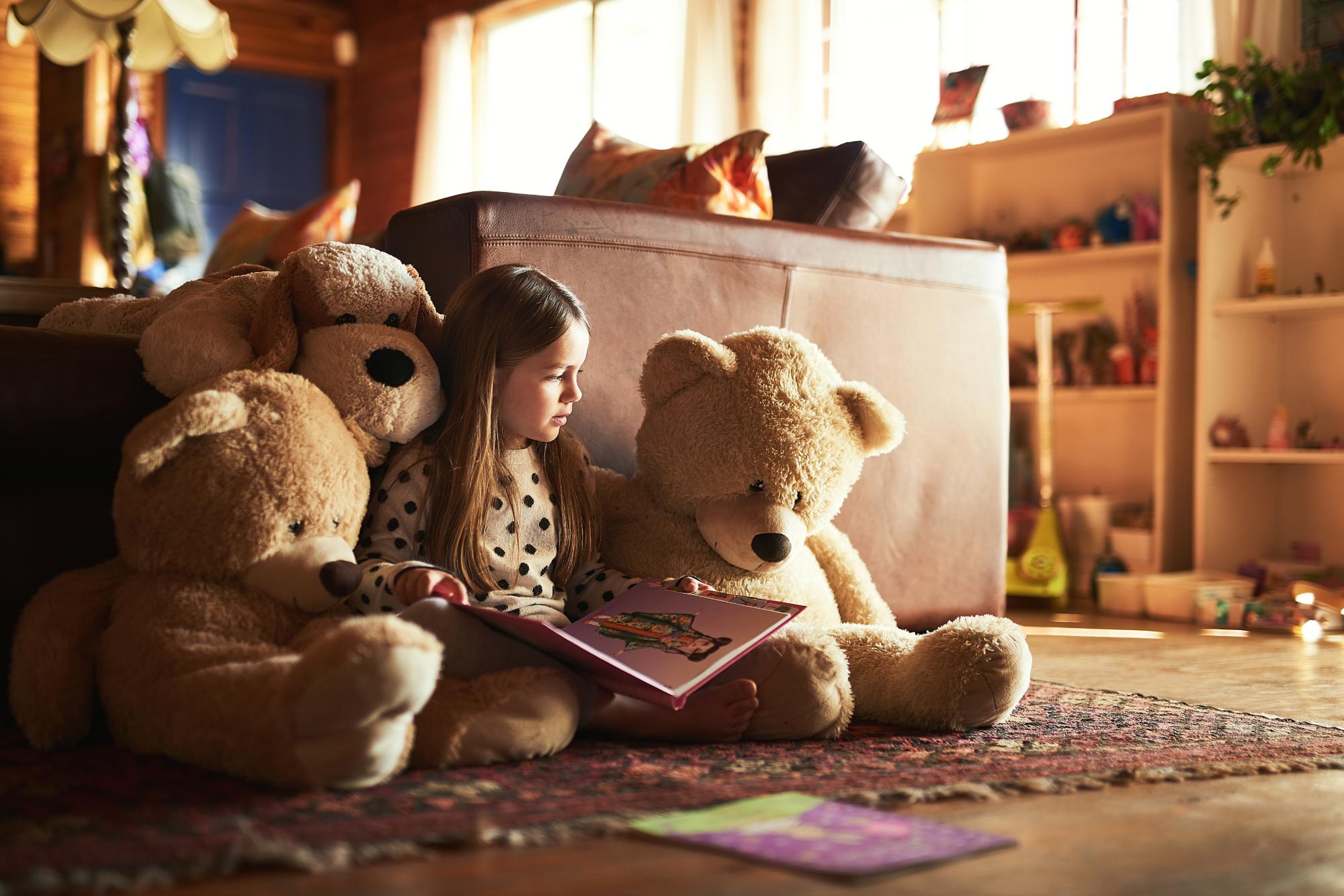 little girl reading a book with her teddy bears