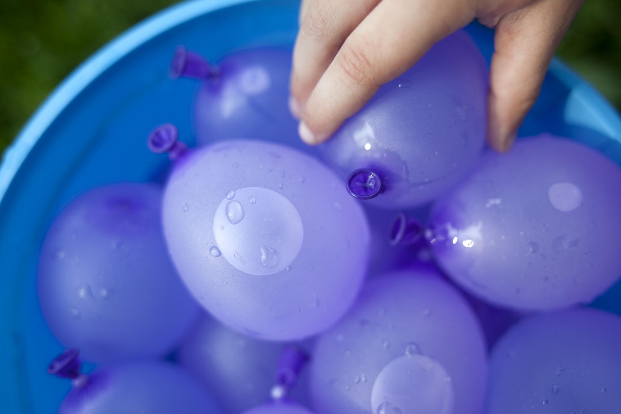 Hand reaching to grab some purple water balloons
