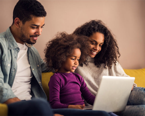 Happy parents and their young daughter using a laptop on a sofa