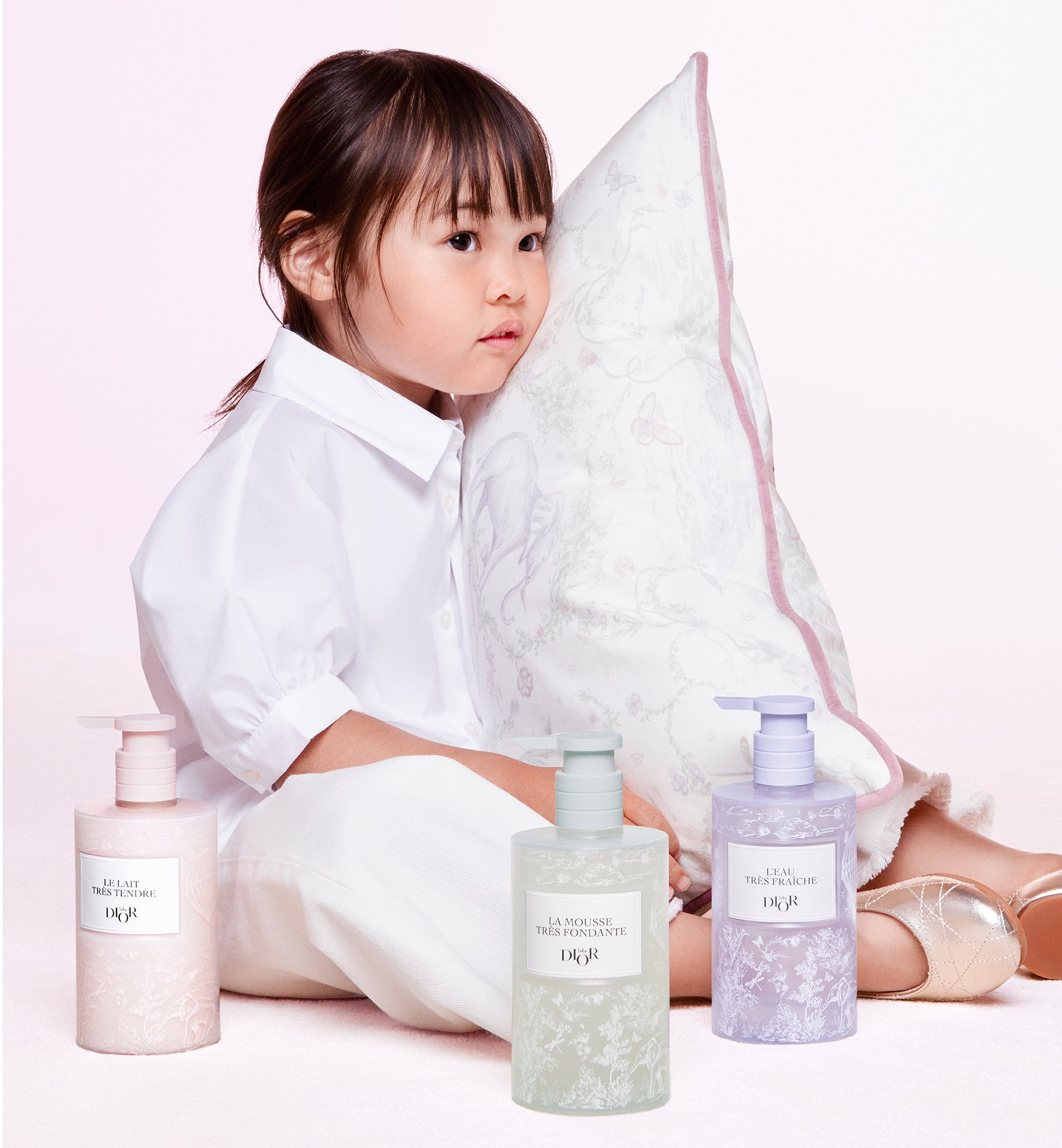 A picture of a little girl lying on a teddy bear blanket looking at Baby Dior baby care.