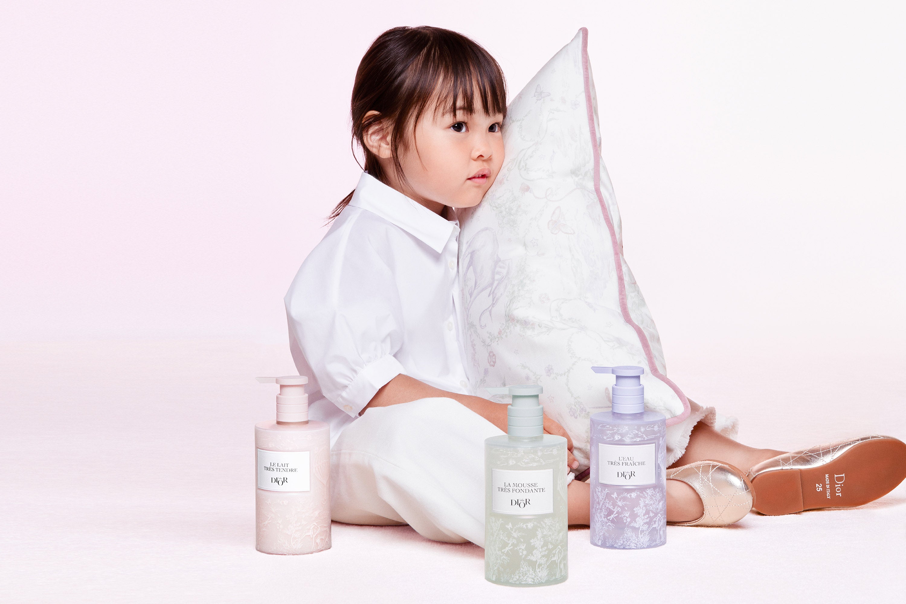 A picture of a little girl lying on a teddy bear blanket looking at Baby Dior baby care.
