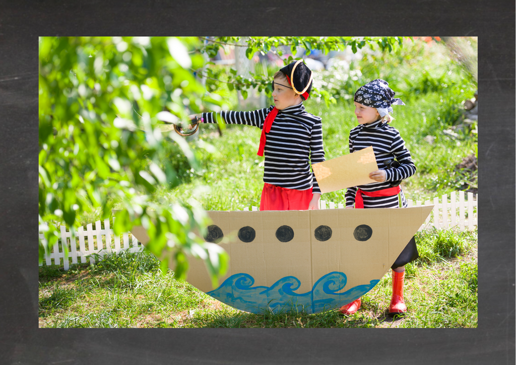Kindergeburtstag Idee: Piraten auf hoher See. Kinder stehen als Piraten verkleidet hinter einem Pappschiff.