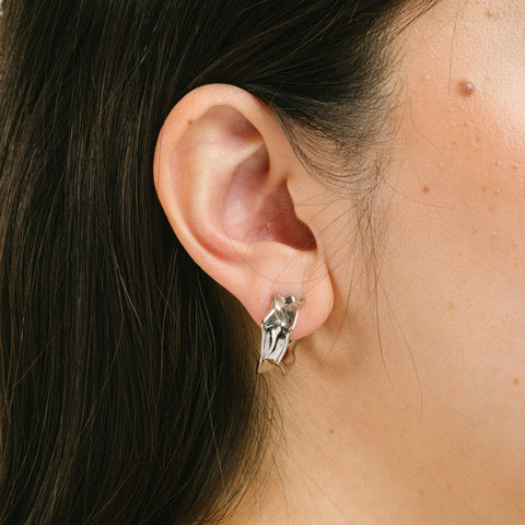 A model wearing the Liquid Melt Hoop Clip On Earrings feature a Mosquito Coil Clip-On closure ideal for all ear types including thick/large ears, sensitive ears, small/thin ears, and stretched/healing ears. On average, they offer a comfortable wear duration of 24 hours and a medium secure hold, with an adjustable fit. Crafted from silver toned copper alloy, each purchase includes one pair of the earrings.