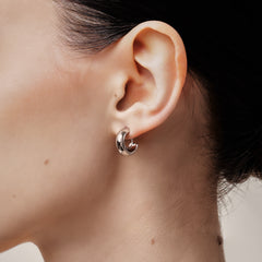 A model wearing the Simple Silver Huggie Clip-On Earrings provide a medium secure hold, making them perfect for all ear types. With adjustable padding for extra comfort, these earrings can be worn for up to 24 hours with ease. Crafted from copper alloy, they are also available in a gold finish.