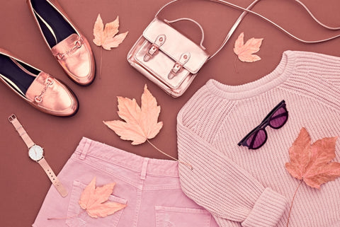 Pink fall outfit pieces laid out on background covered with leaves