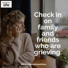 A woman is listening to someone on the phone while looking out a window. Text: Check in on family and friends who are grieving. #WorldMentalHealthDay