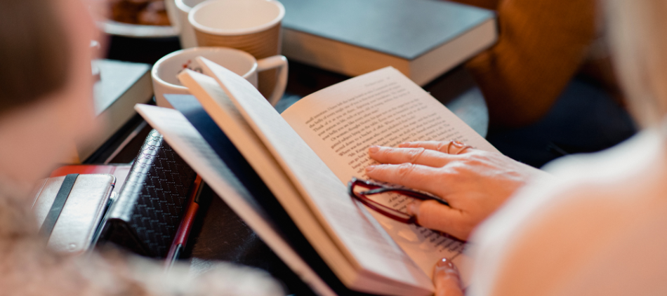 Looking over the shoulder at a person&#039;s hand on the pages of a book