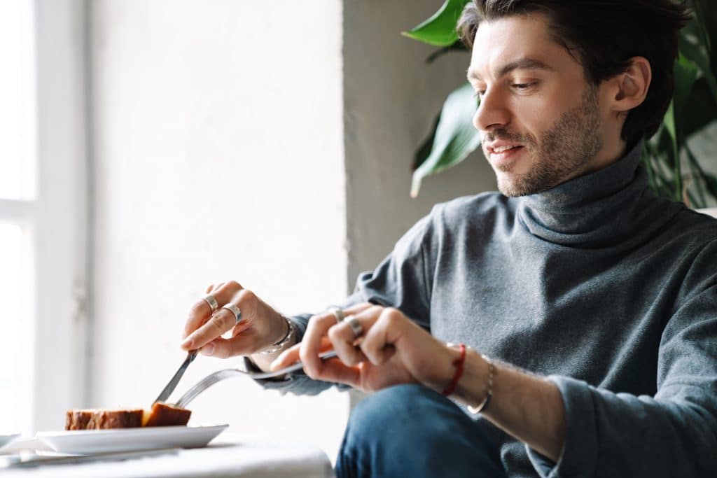 handsome man eating dessert while having breakfast in cafe