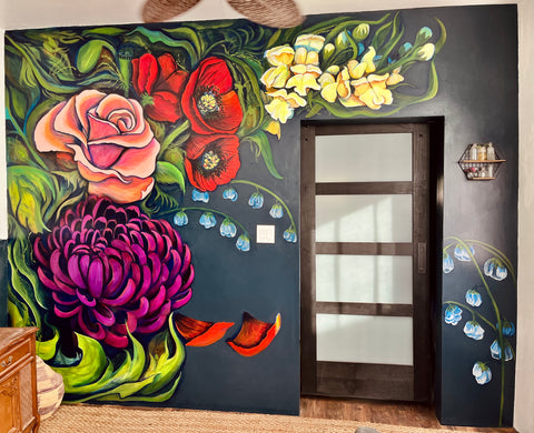 A floral mural by Roxy Tocin, on a navy blue wall, featuring a purple mum, crimson poppies, pink and gold rose, and yellow snap dragons with white snowbells
