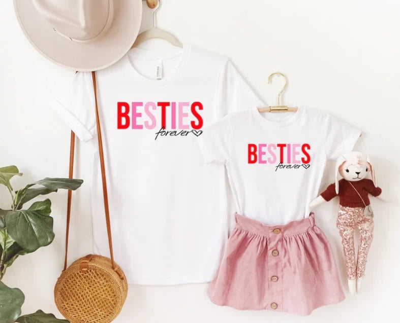 Mommy and me shirts with 'Besties forever' printed on it. Accessories in the image are a hat, woven bag, and a