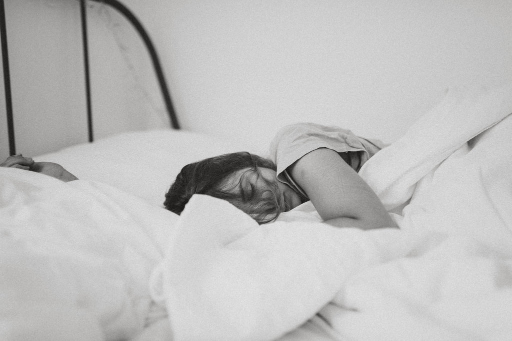 A black and white photo of a woman sleeping in bed with a white pillow and blanket